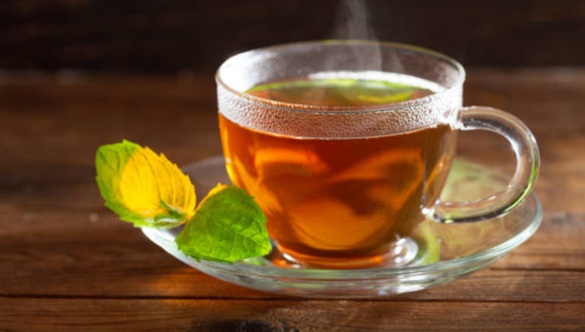 A steaming cup of Vacia Detox Tea with a mint leaf on a wooden table.