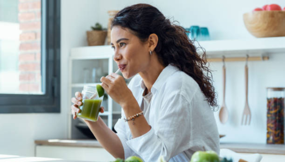 Woman drinking a Pure Body Detox green smoothie in kitchen